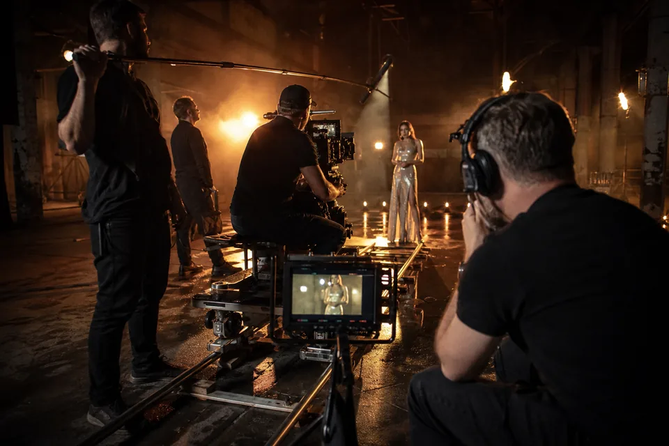 Music video shoot at night with a director, camera crew and a performer in a silver dress under stage lights