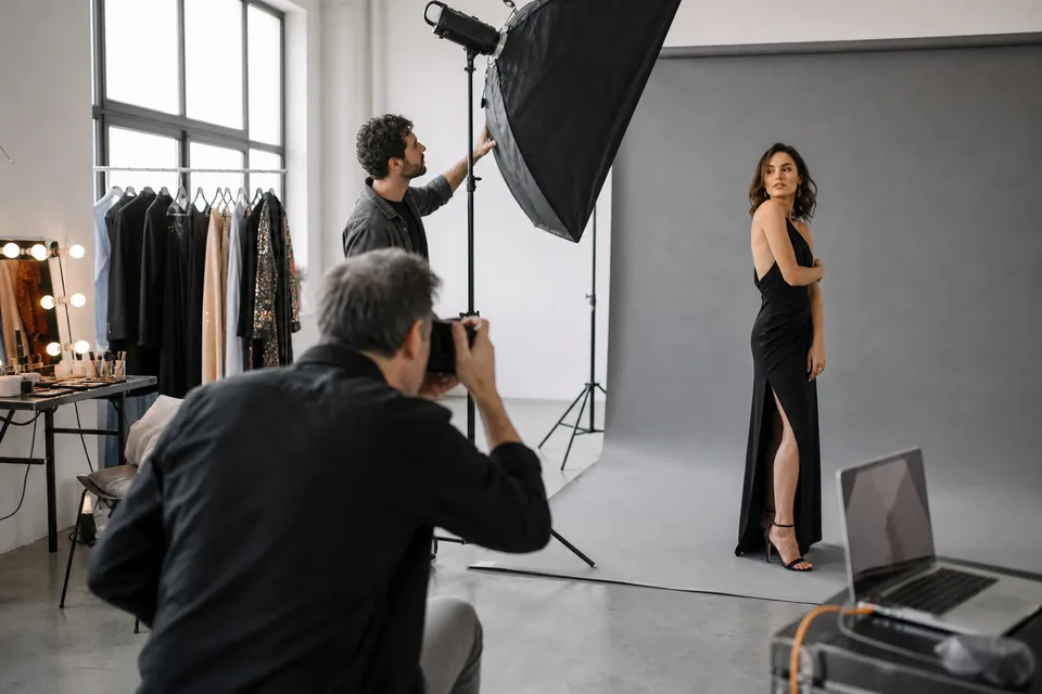 Photographer and assistant adjusting a softbox around a performer in a black evening dress on a seamless studio backdrop